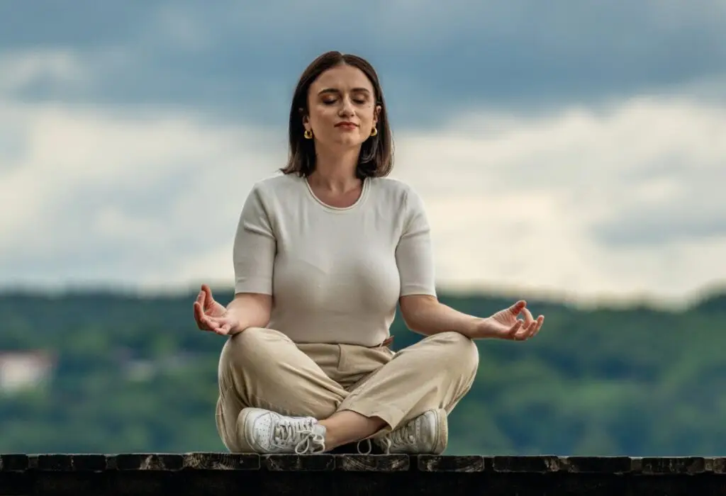 Monica Matrella von the birth circle with Monica sitzt im Schneidersitz auf einer Steinmauer und meditiert. Mit geschlossenen Augen, entspanntem Gesichtsausdruck und ruhiger Haltung wirkt sie gesammelt und zentriert.